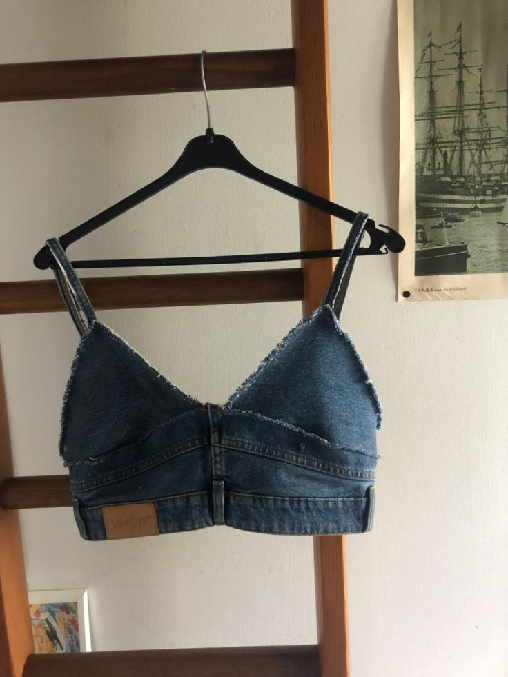 a denim bra hanging on a clothes rack in front of a wall with an old photo