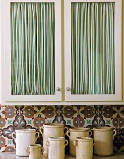 some pots are sitting on the counter in front of two cupboards with green curtains