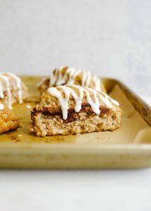 three pastries with icing sitting on a yellow plate next to a wooden spoon