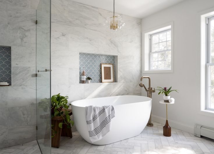 a white bath tub sitting in a bathroom next to a window and potted plants