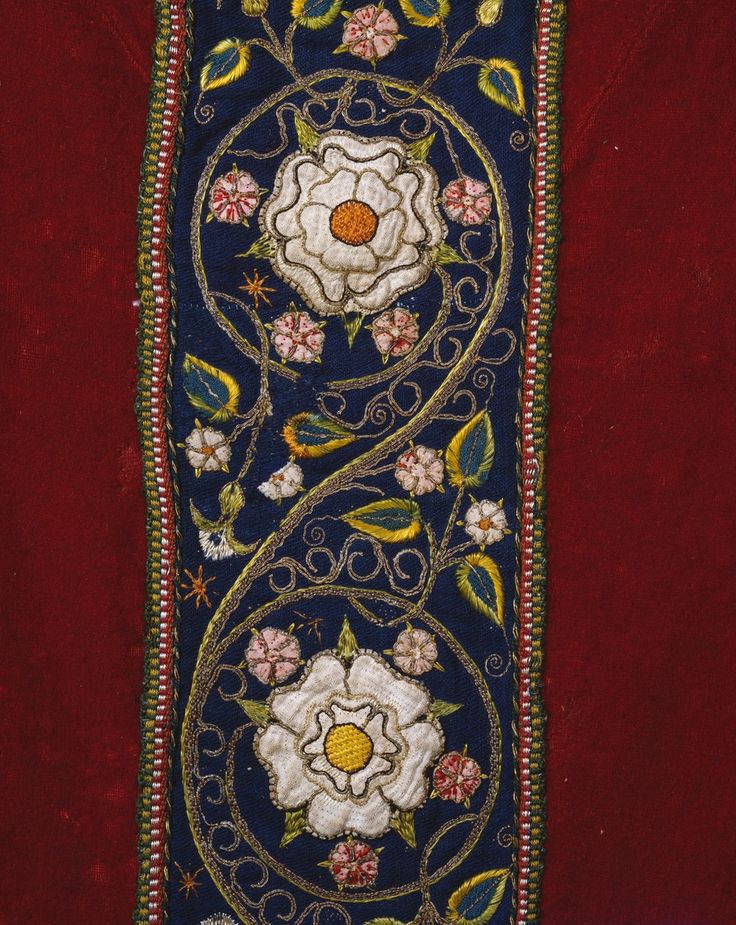 an embroidered bookmark with flowers and leaves on red velvet, hanging from a wall