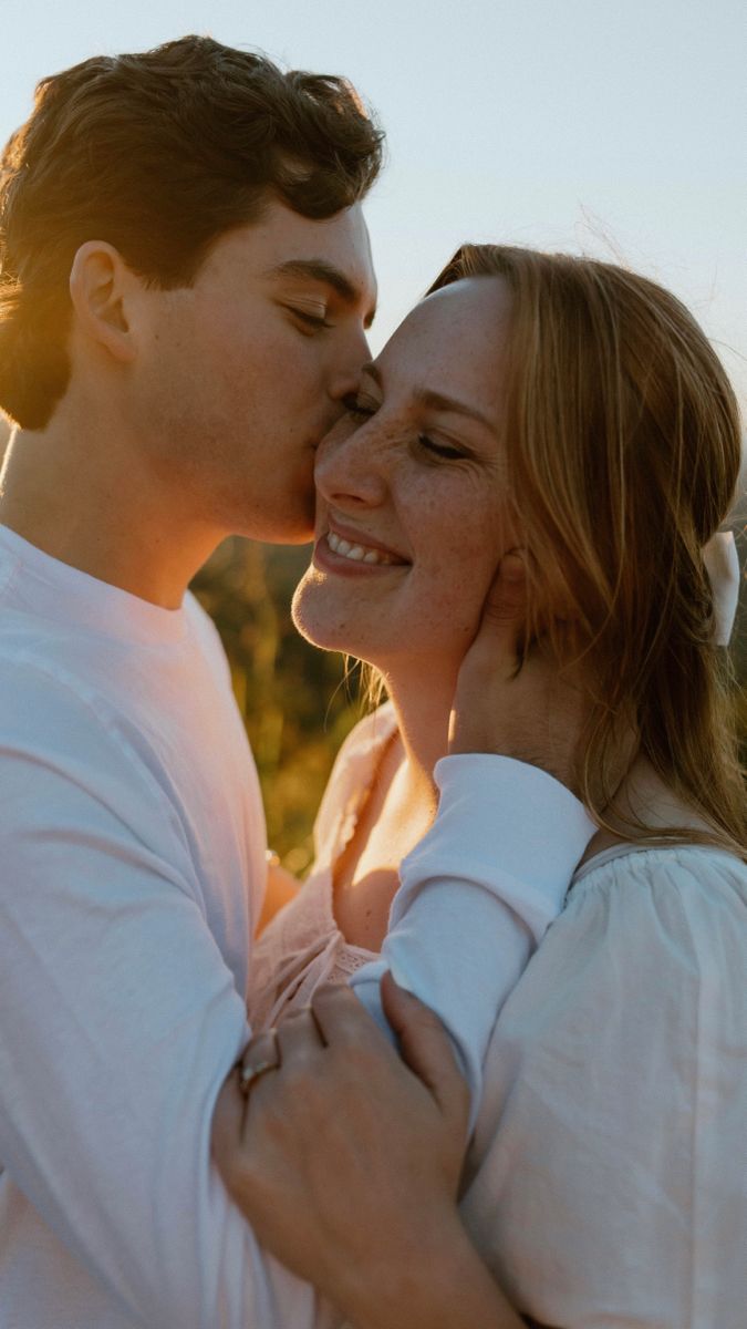 a young man and woman kissing each other while the sun shines in the background