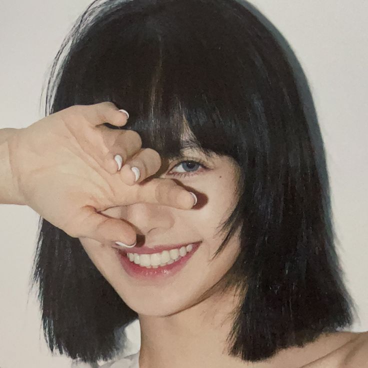 a woman with short black hair holding her hand up to her face and smiling at the camera