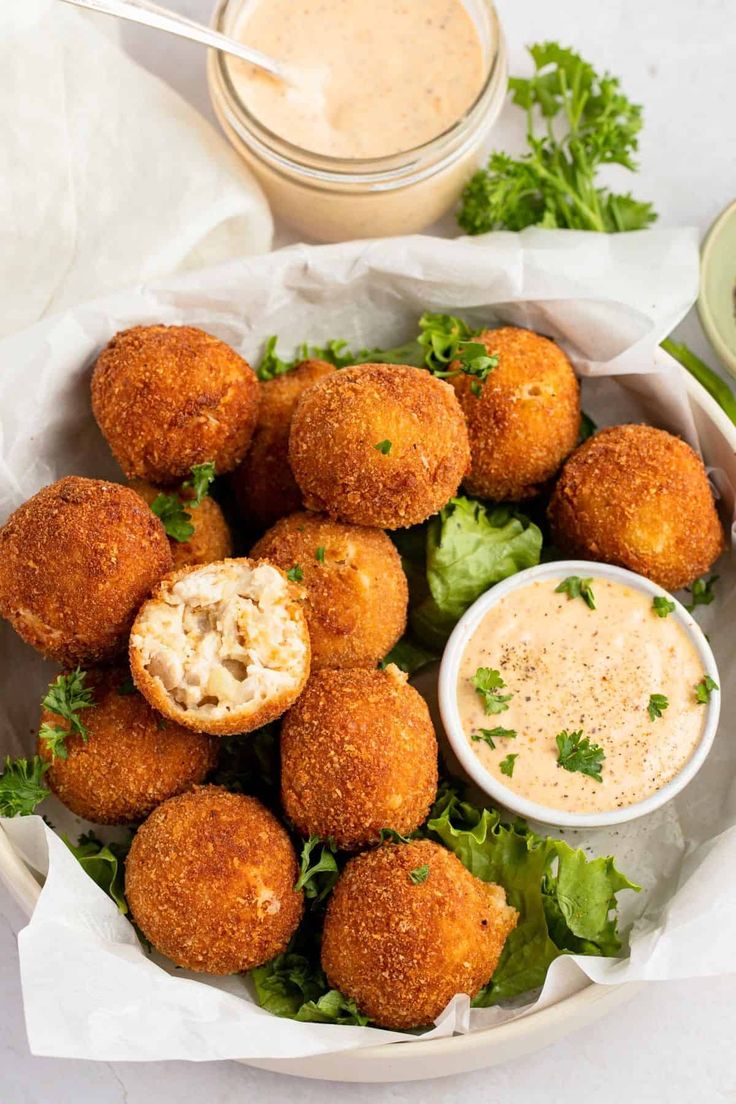 a white bowl filled with fried food and dipping sauce on top of lettuce