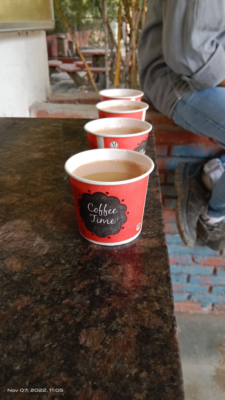 three cups of coffee sitting on top of a counter next to a person's feet