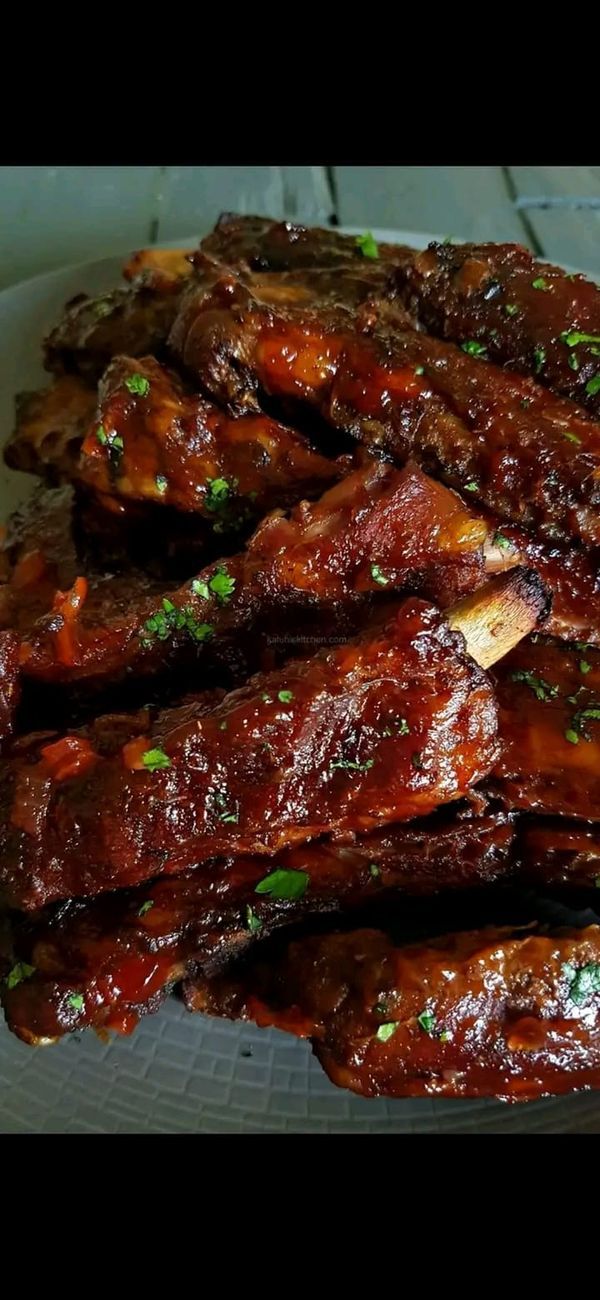 ribs covered in barbecue sauce and garnished with parsley on a white plate