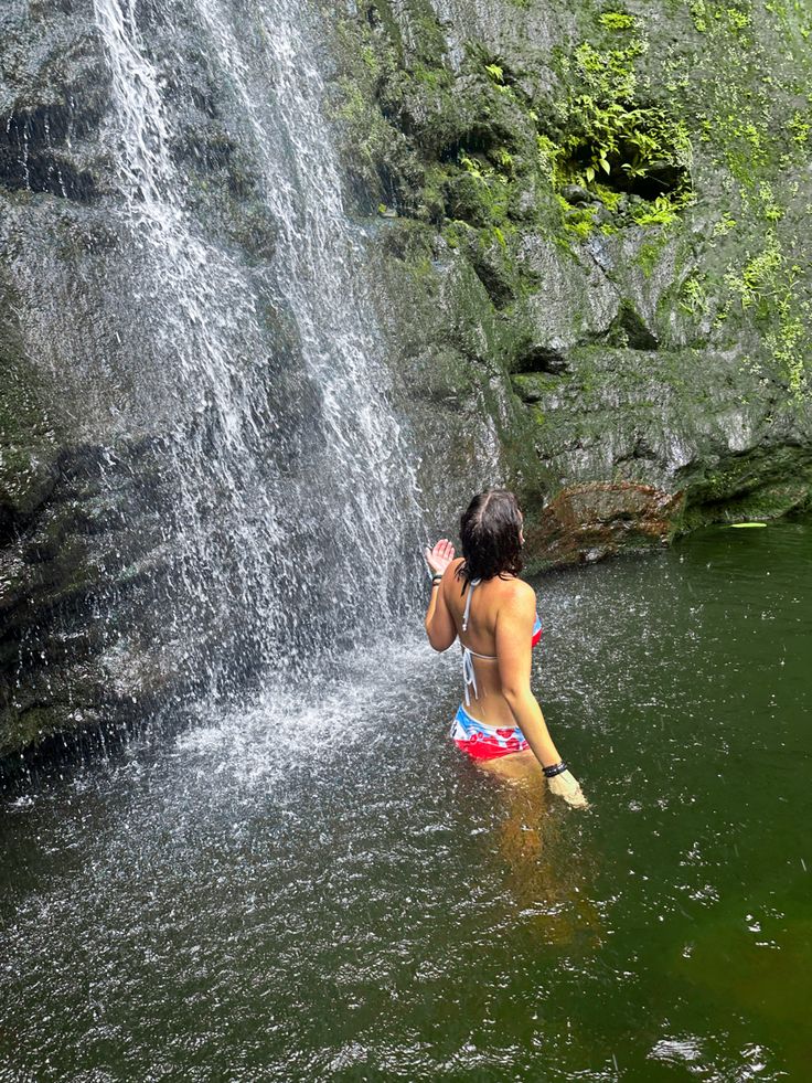 a woman standing in the water next to a waterfall