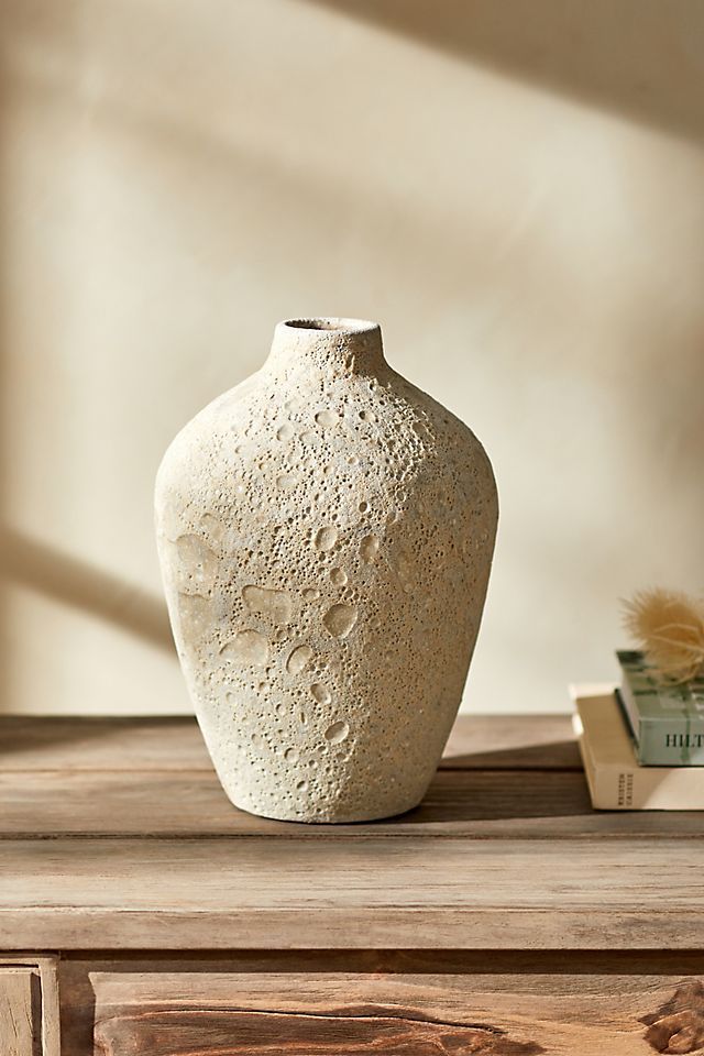 a white vase sitting on top of a wooden table next to a bookshelf