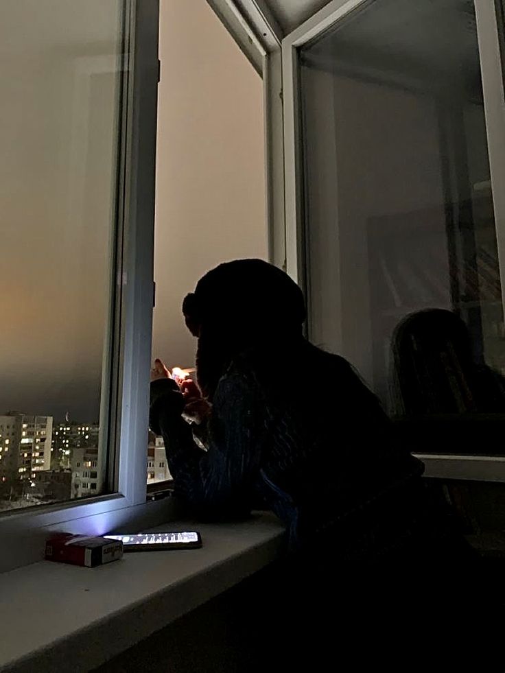 a person sitting on a window sill looking out at the city lights in the distance