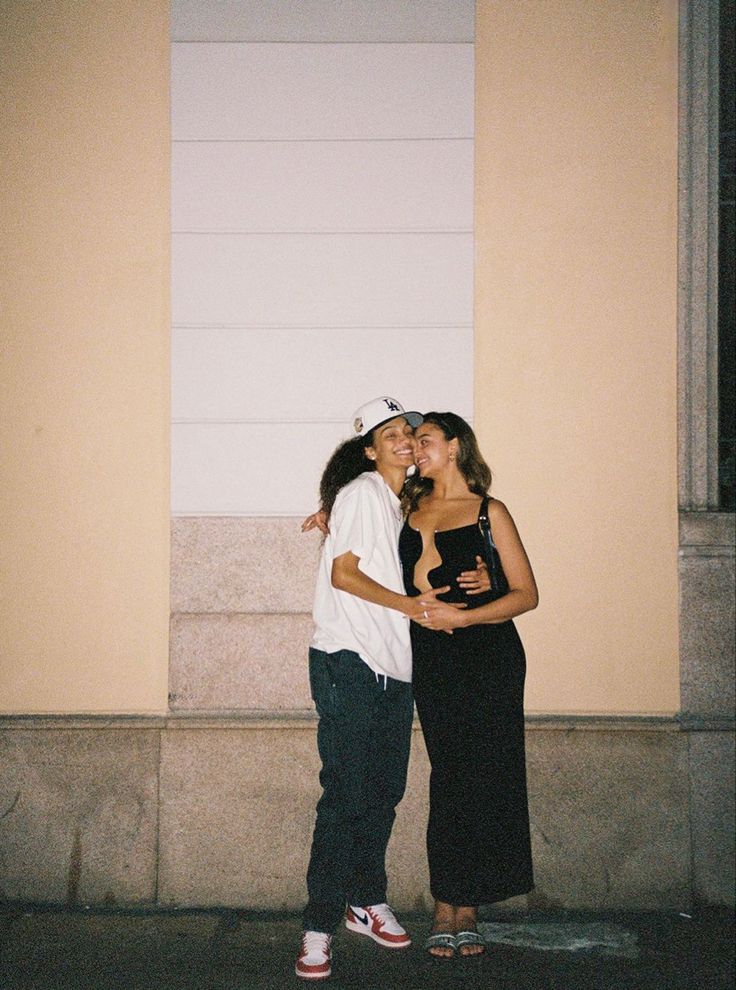 two women standing next to each other in front of a building