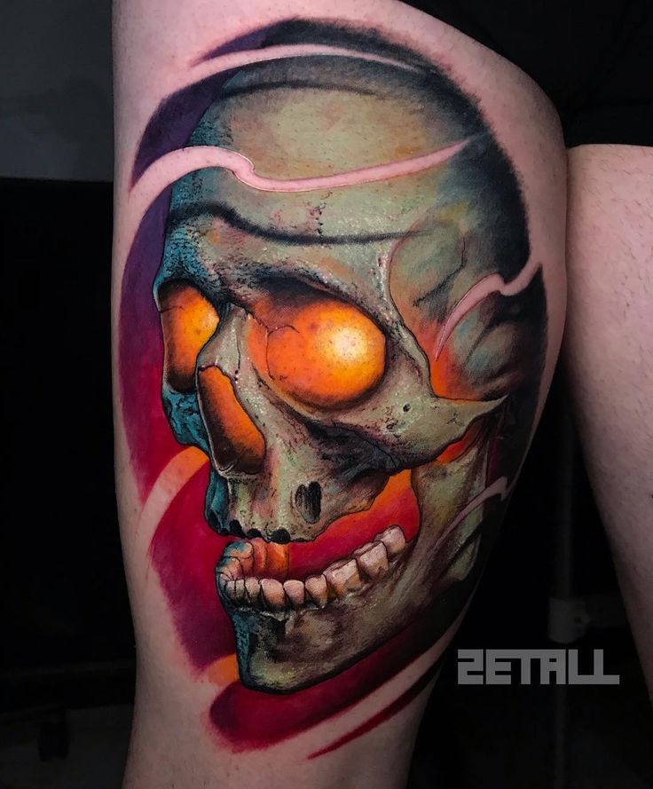 a man's thigh with a skull and orange eyes tattoo on his leg,