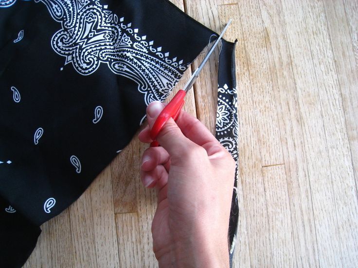 a person cutting fabric with scissors on a wooden table next to a black bandana