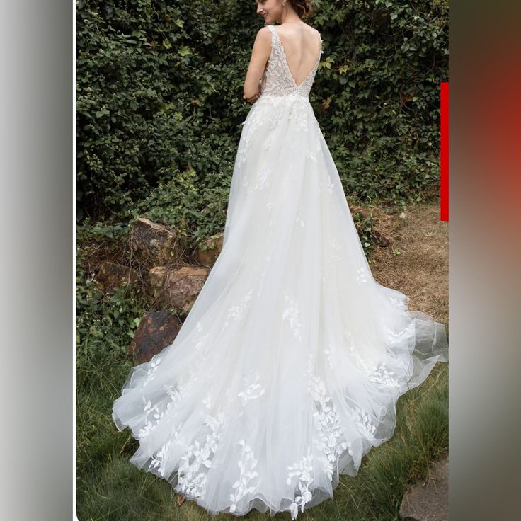 a woman in a white wedding dress standing on grass with bushes behind her, looking off into the distance