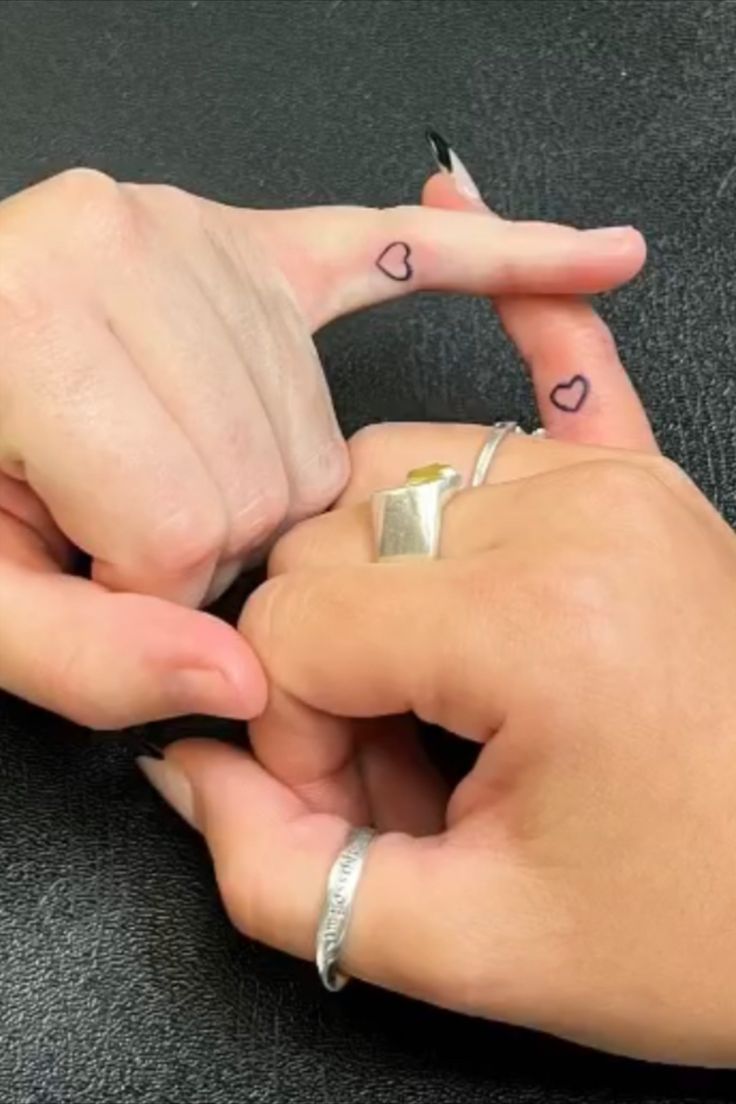 two people holding hands with hearts tattooed on their thumbnails and fingers pointing at each other