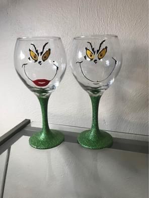 two wine glasses with faces painted on them sitting next to each other in front of a white wall