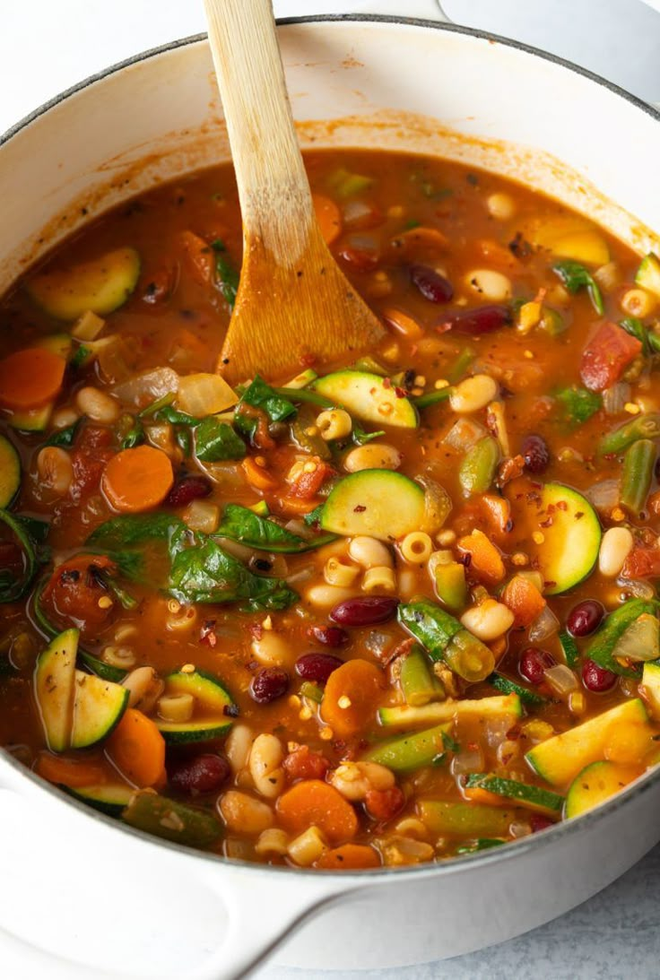 a pot full of vegetable soup with a wooden spoon