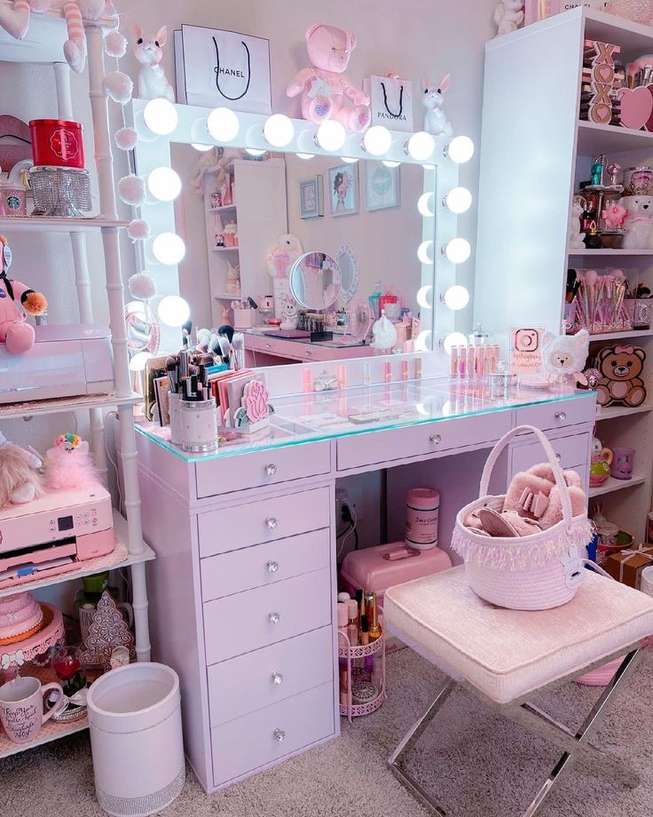 a pink vanity with lights on it and a teddy bear sitting in the chair next to it