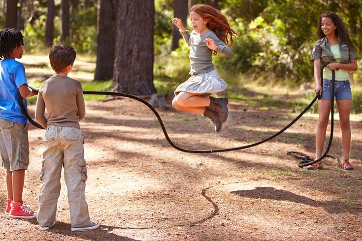 three children are playing with a rope in the woods while another child is jumping up into the air