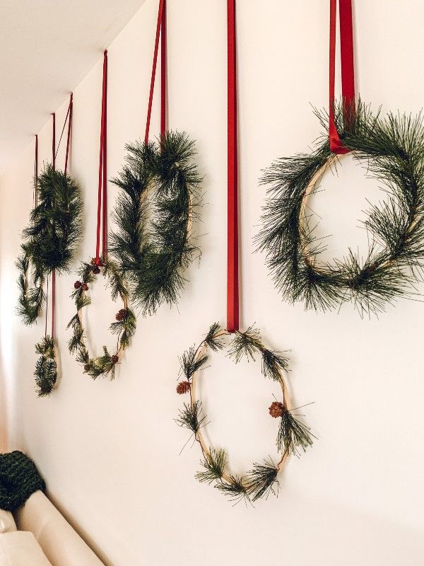 christmas wreaths hung on the wall with red ribbons and pine cones hanging from them