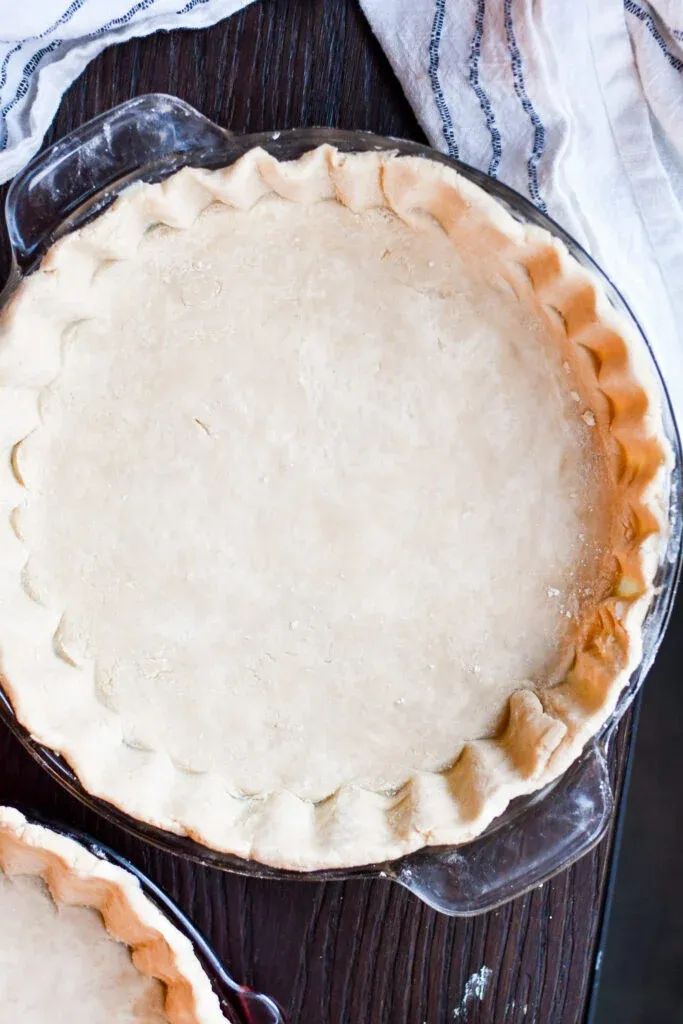 two pie crusts sitting on top of a wooden table next to each other,