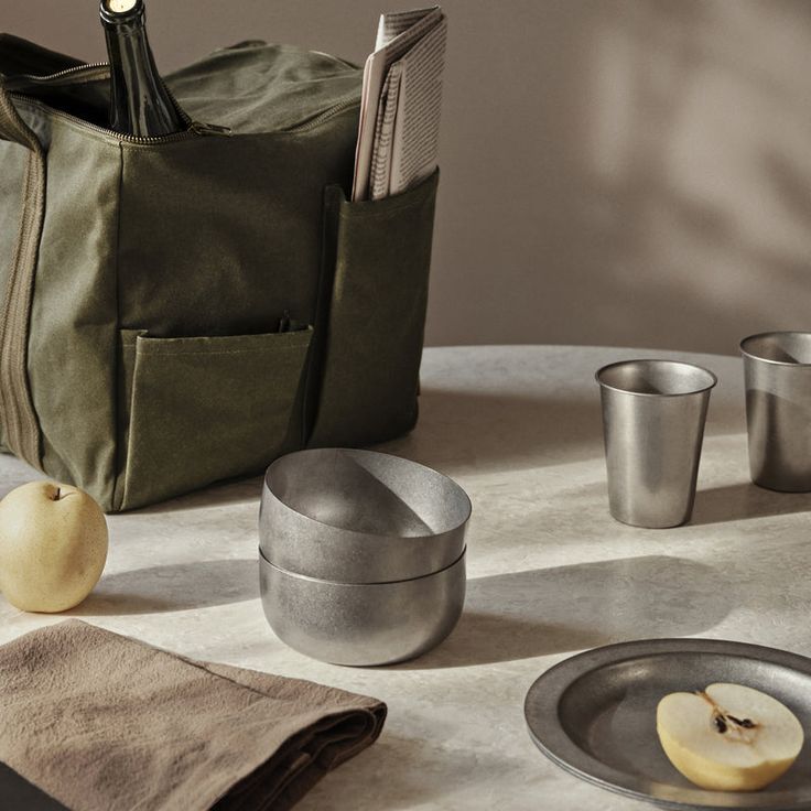 a table topped with metal cups and silverware next to an apple on top of a plate