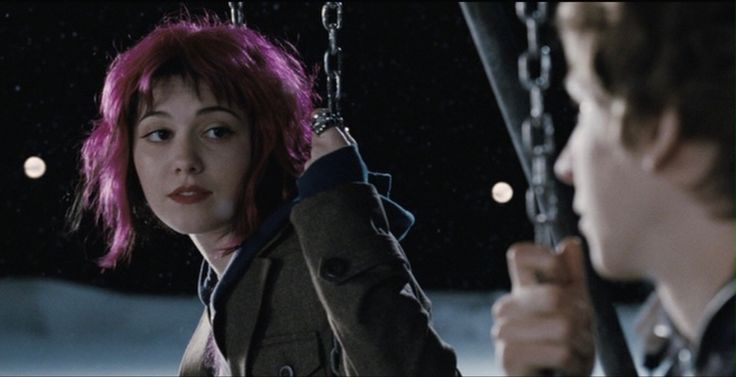 a woman with pink hair sitting on a swing next to a man in a suit