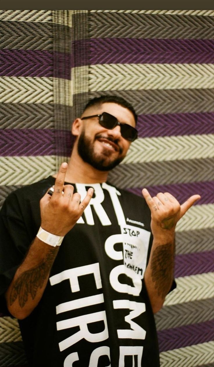 a man in sunglasses and a t - shirt with the word fire on it is standing next to a wall