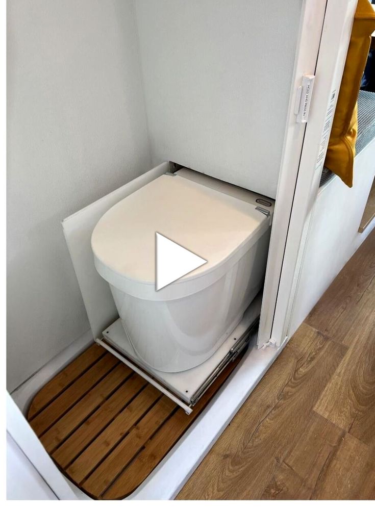 a white toilet sitting on top of a wooden floor next to a doorway with a yellow pillow