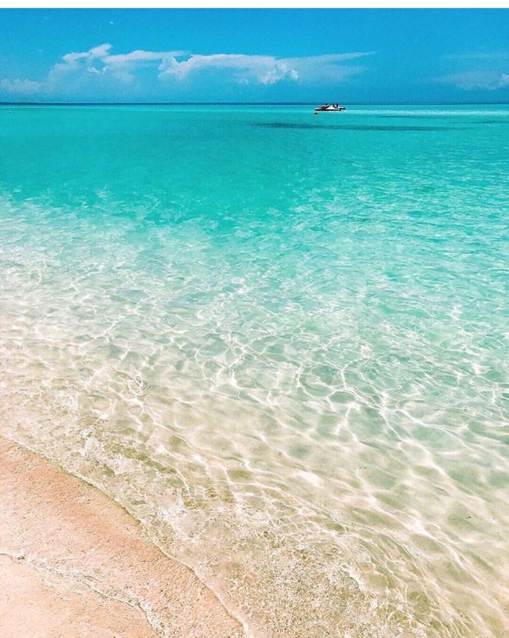 the water is crystal blue and clear with white sand on the beach, as well as a boat in the distance