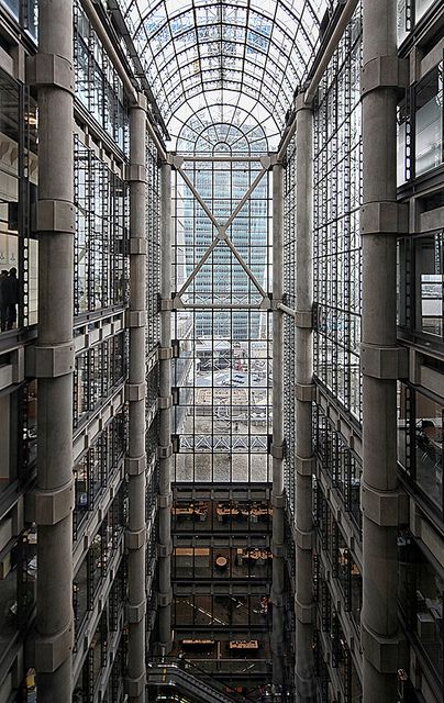 the inside of a building with lots of glass and metal structures on each floor, looking up at the sky