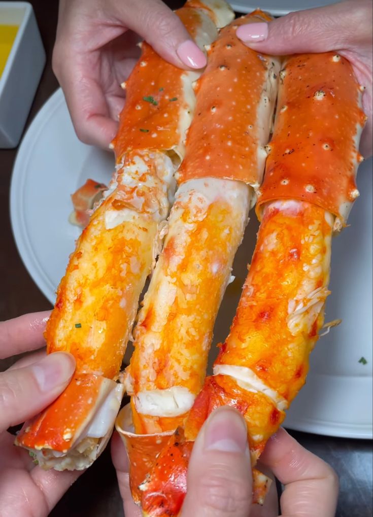 two hands are holding some crab legs on a plate with other plates in the background