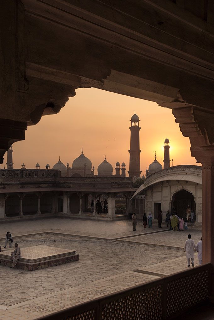 the sun is setting over an old building with people walking around in front of it