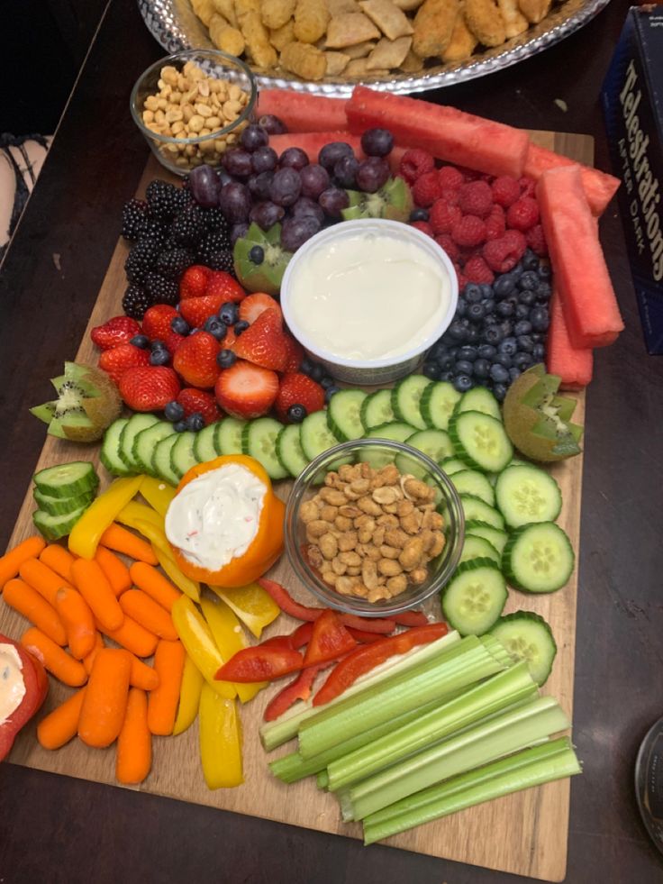 a wooden cutting board topped with fruits and veggies next to bowls of dip