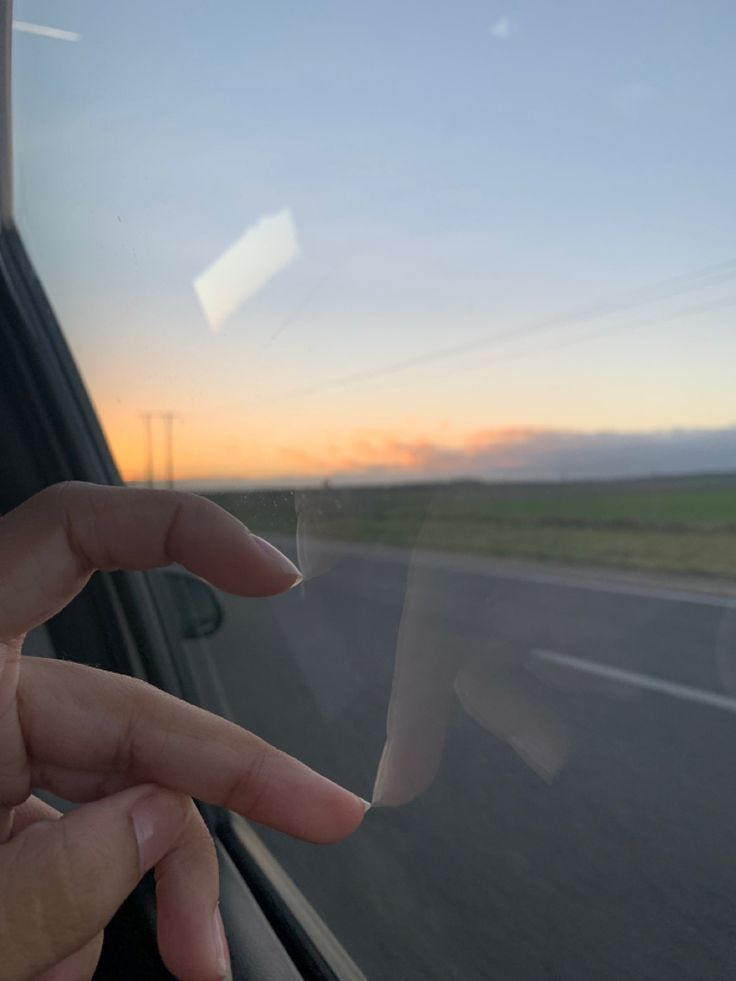 a person's hand on the window of a car as the sun goes down