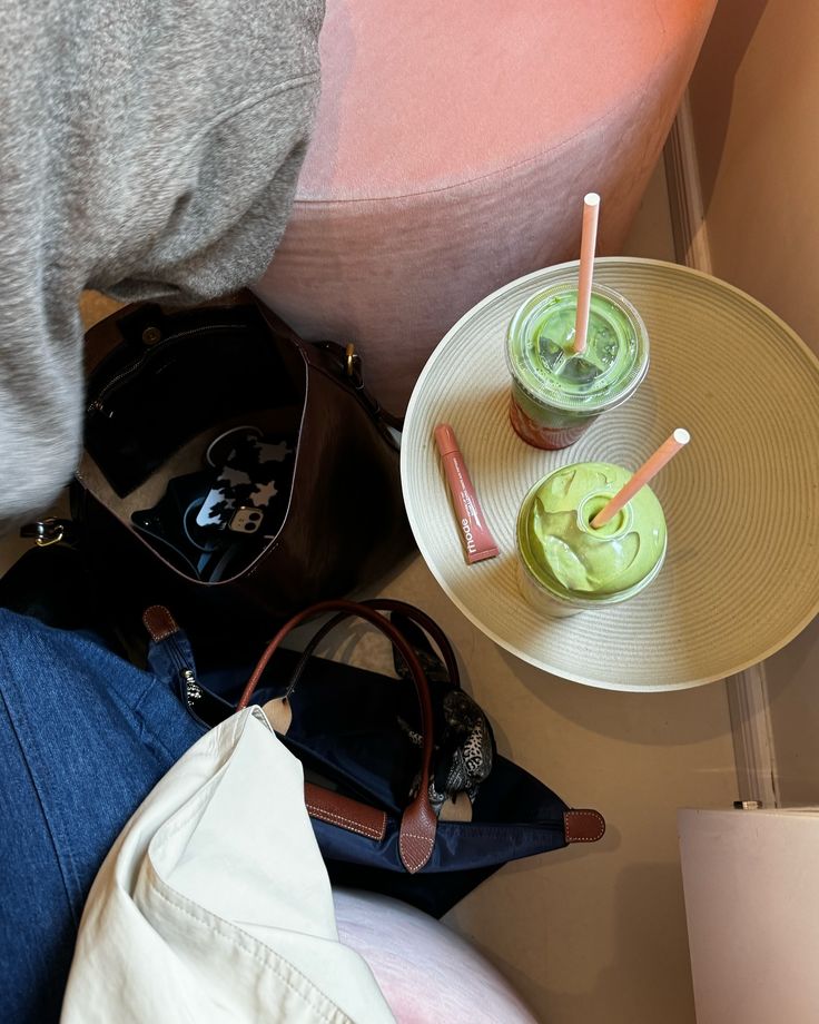 two drinks are sitting on a table next to a handbag and purse, along with other items