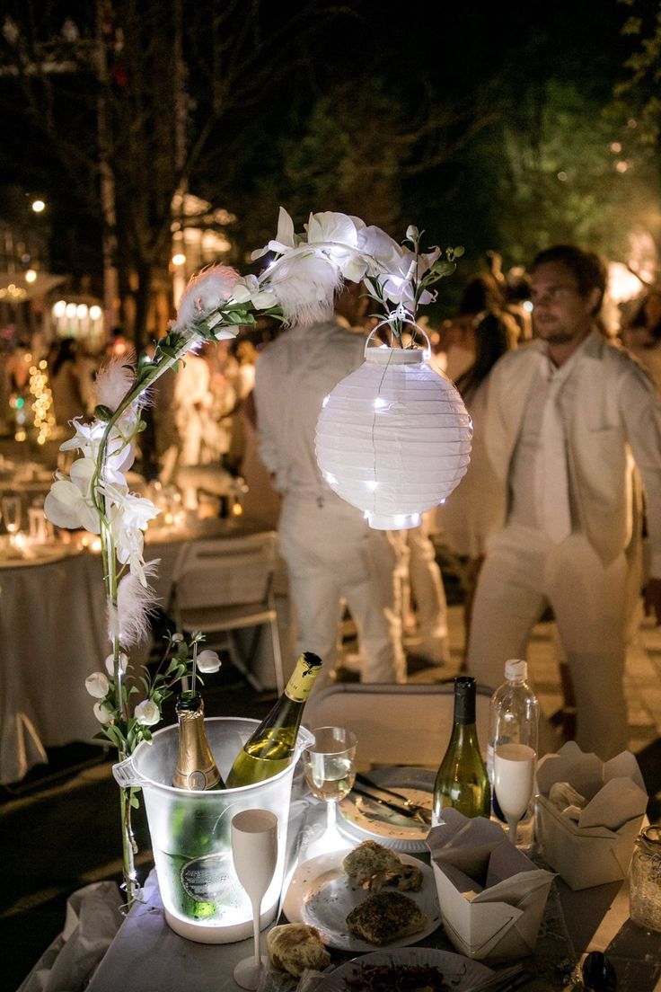 a table topped with wine bottles and plates filled with food next to people standing in the background