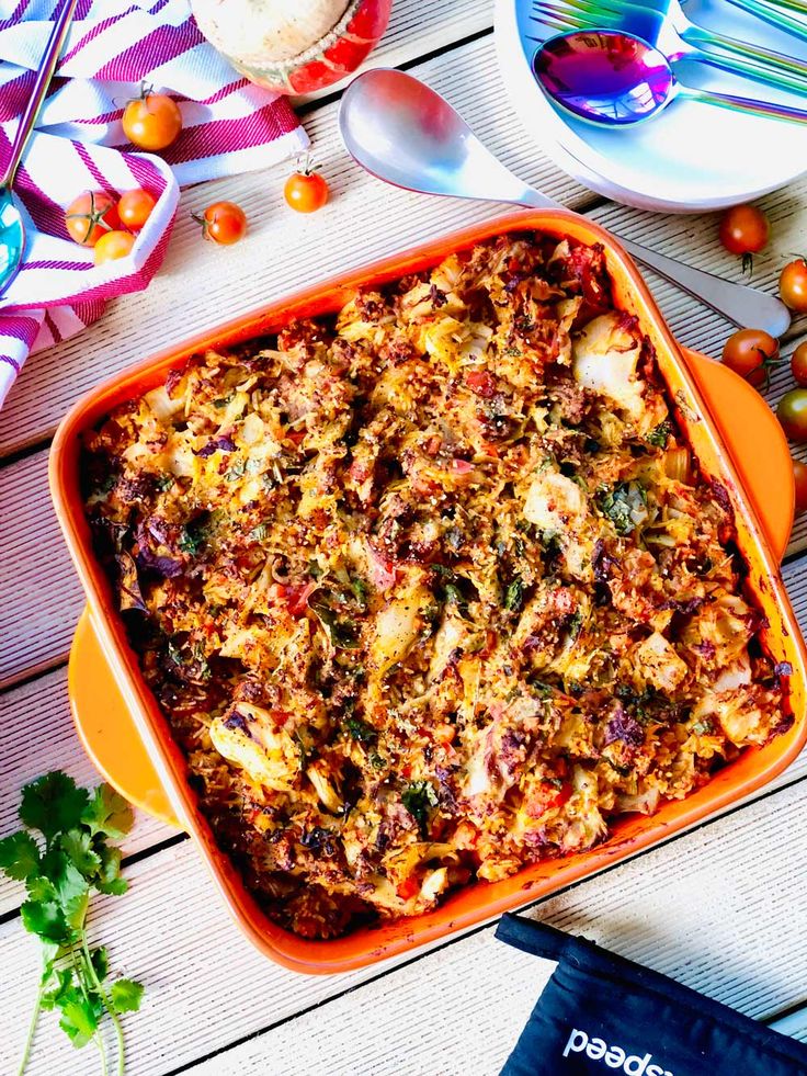 an orange casserole dish with meat and vegetables in it on a wooden table