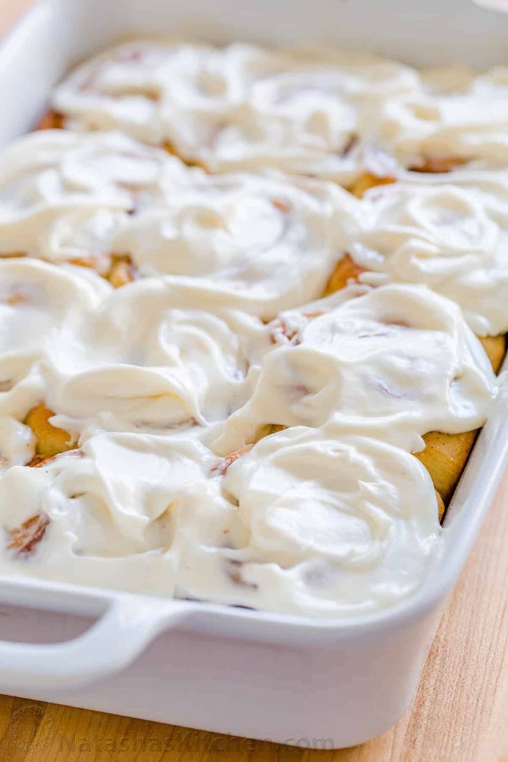 a casserole dish with white icing and cinnamon rolls in it on a wooden table