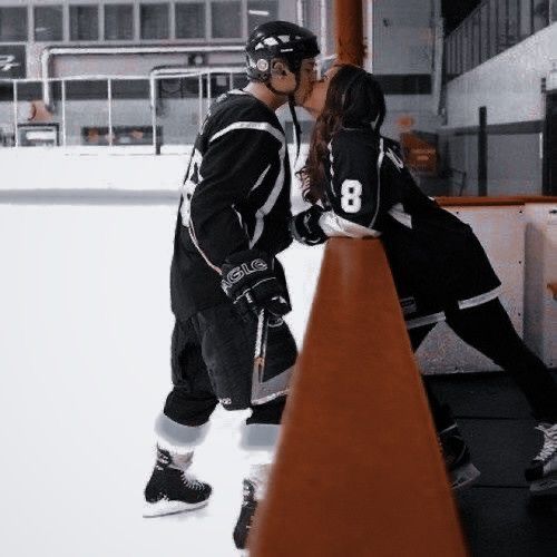 two people in black and white are kissing on the ice rink while one person is wearing skis