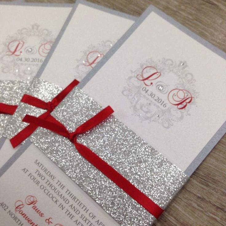 three silver and red wedding cards with ribbon on them, sitting on top of a wooden table