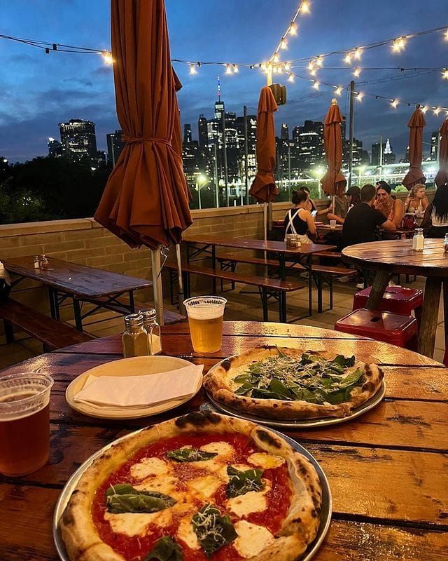 two pizzas sitting on top of a wooden table next to beer glasses and umbrellas