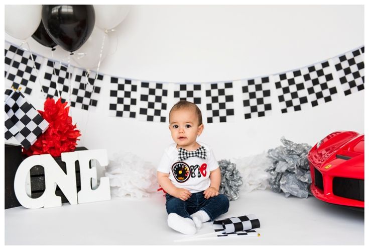 a baby sitting on the floor in front of a race car backdrop