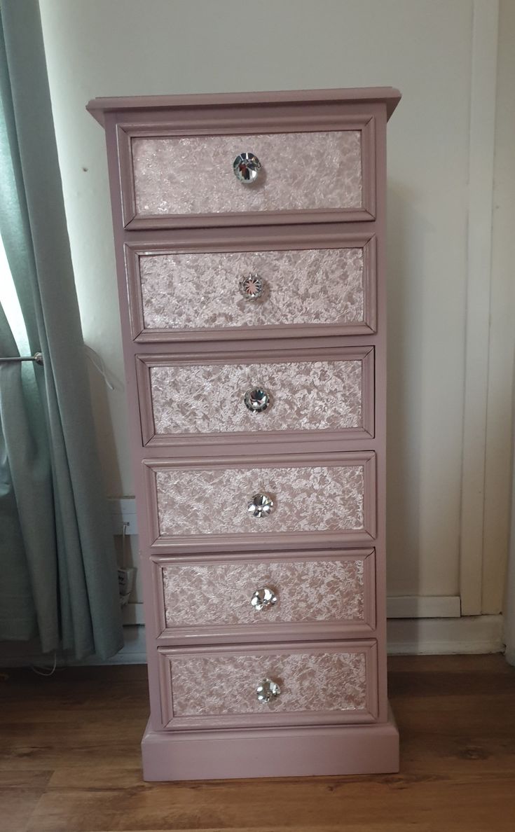 a pink chest of drawers sitting on top of a wooden floor next to a window