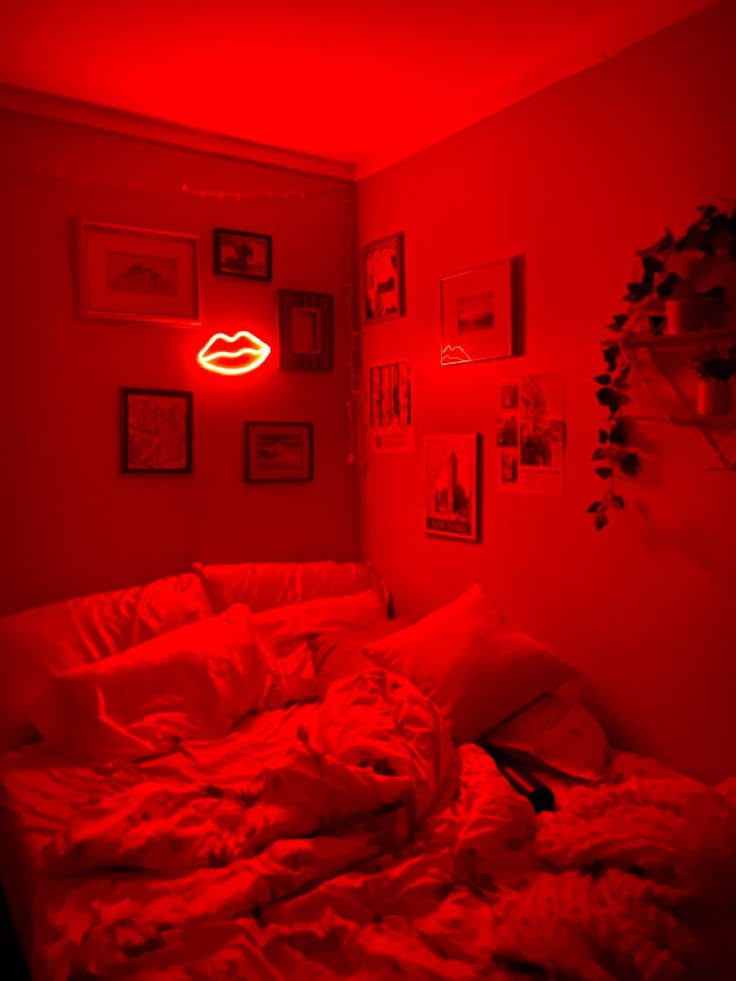 a bedroom with red light coming from the ceiling and pictures on the wall above it