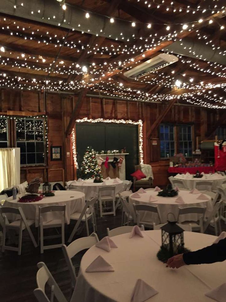 a room filled with tables covered in white tablecloths and christmas lights hanging from the ceiling