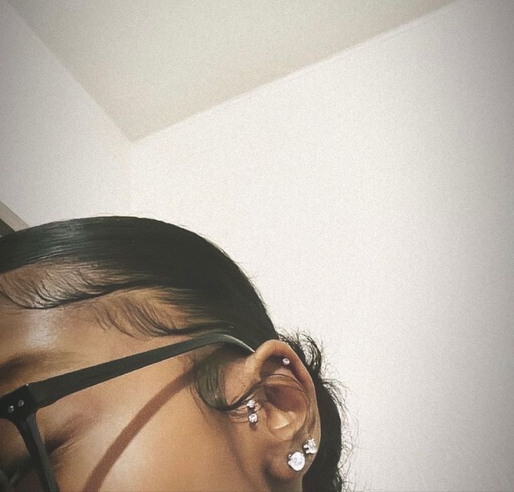 a woman wearing black glasses with her hair tied back and ear piercings in front of her face