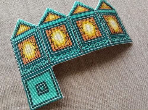 a cross stitched brooch with an image of a building on it's side