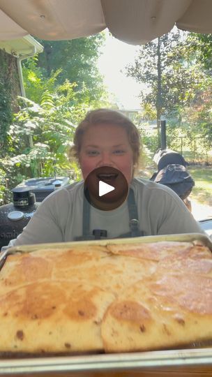 a woman sitting in front of a large pan filled with food on top of a table