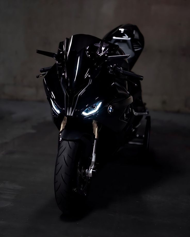 a black motorcycle is parked in a dark room with its lights on and it's headlight turned on