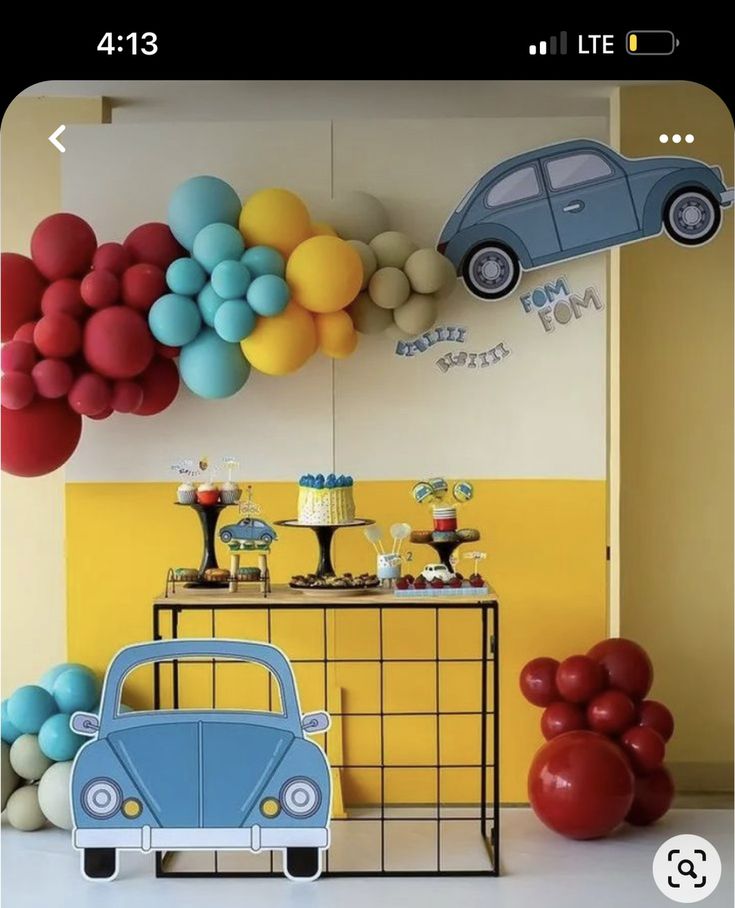 a blue car is parked in front of balloons on the wall and an orange balloon behind it